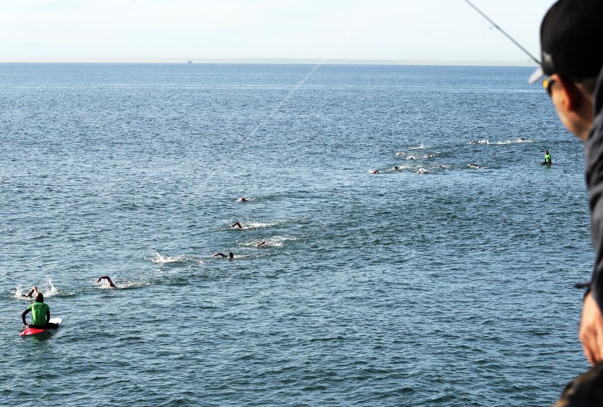 A fisherman on the Newport Beach pier watches as prospective lifeguards compete.