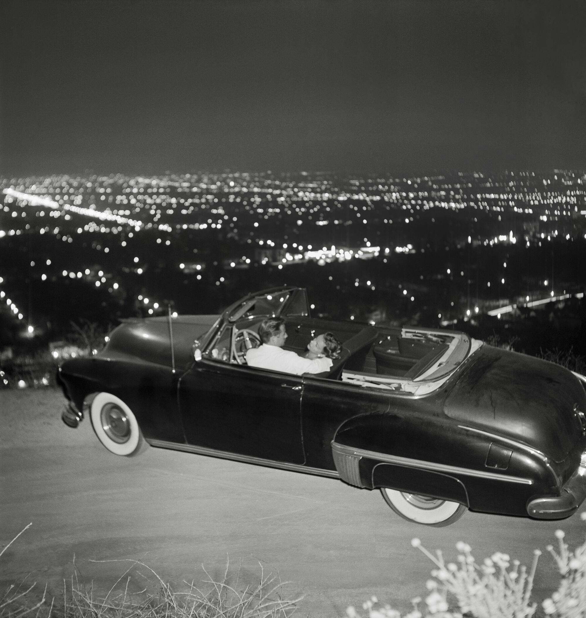 A couple in a convertible overlooking L.A. at night in a historical photo 