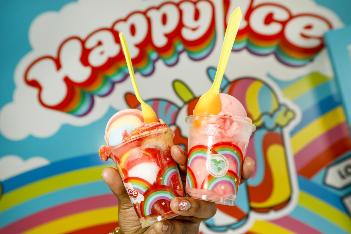 Two cups of fruit ice held up in front of the Happy Ice sign with clouds and rainbows