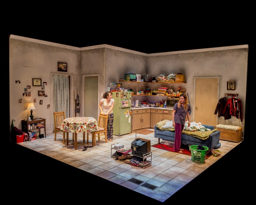 Two women are seen on stage in a set that evokes a working-class apartment