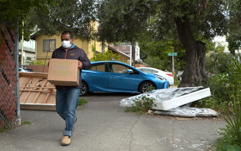 Prem Pariyar, in a mask, walks along a sidewalk carrying a cardboard box.