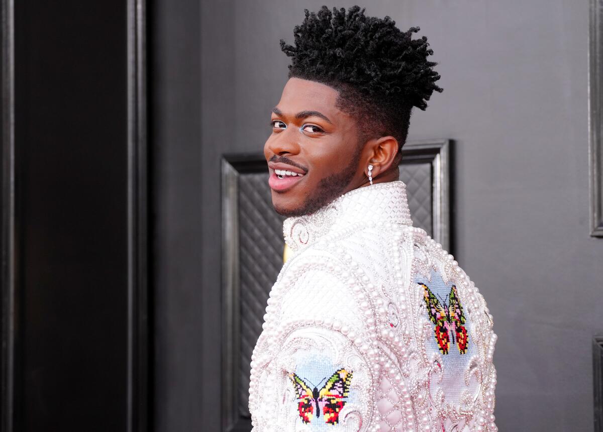  Lil Nas X smiling over his shoulder wearing pearl-studded coat with butterfly stitching 