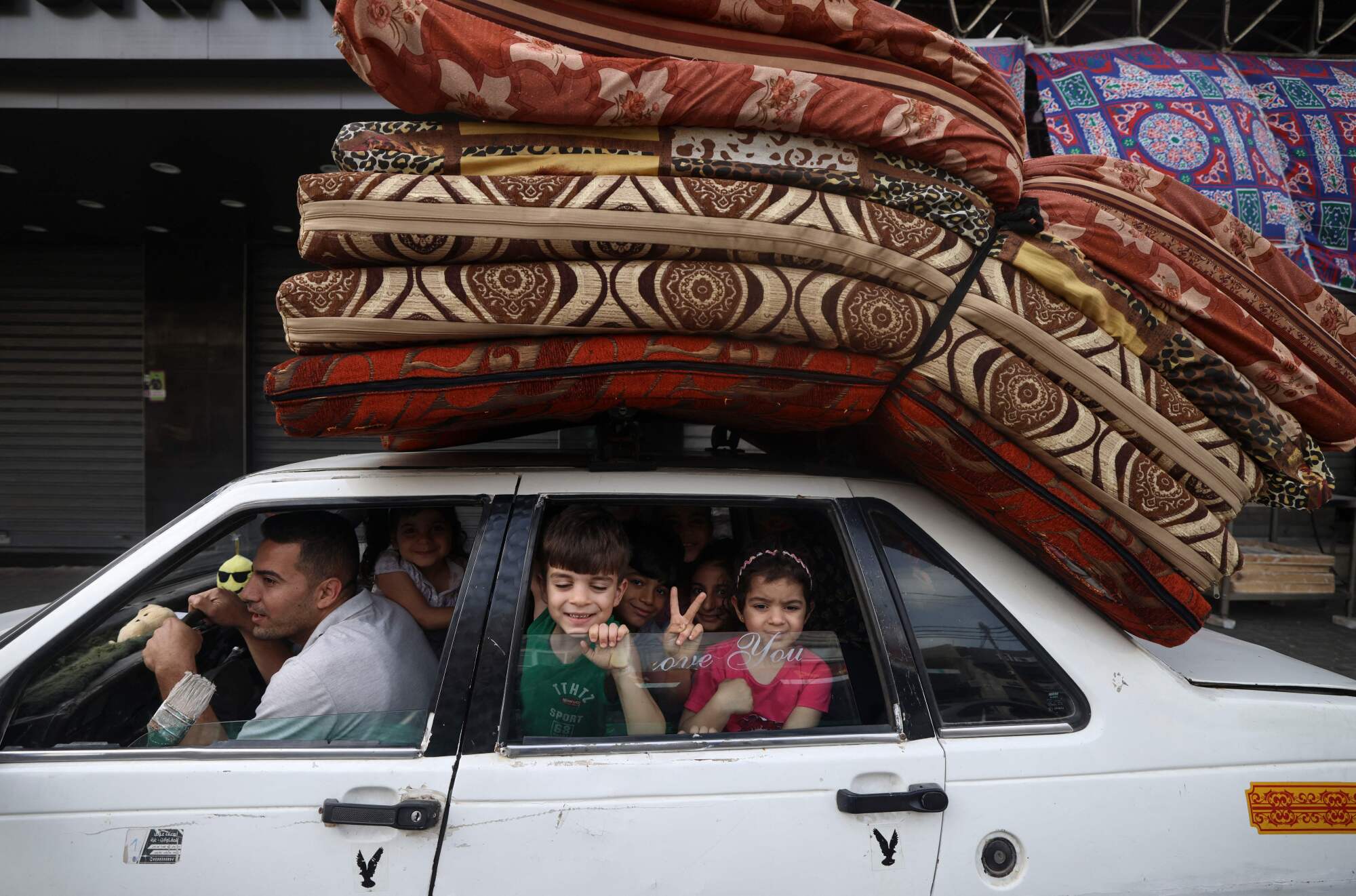 A child flashes the V for victory sign from the back of a family's packed car