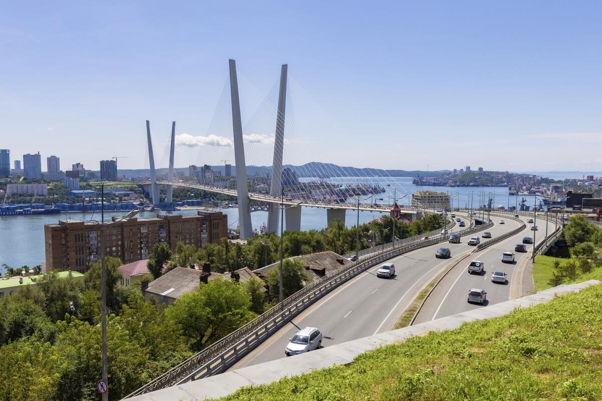 A view of a bridge across a waterway, with buildings on land on left, and cars on roads on the right