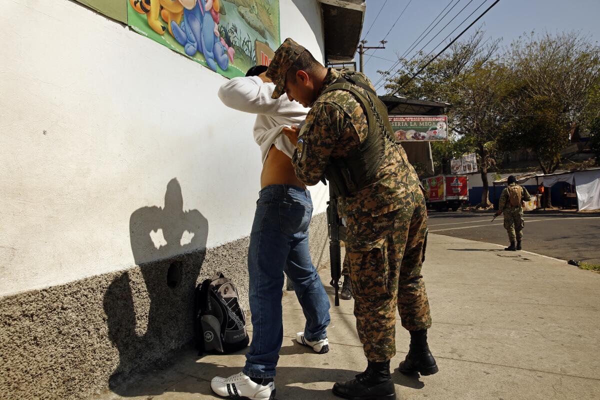 An armed soldier checks a man for gang-related tattoos. The military and police are working together to curb the gang problem, routinely stopping and frisking people. (Carolyn Cole / Los Angeles Times)