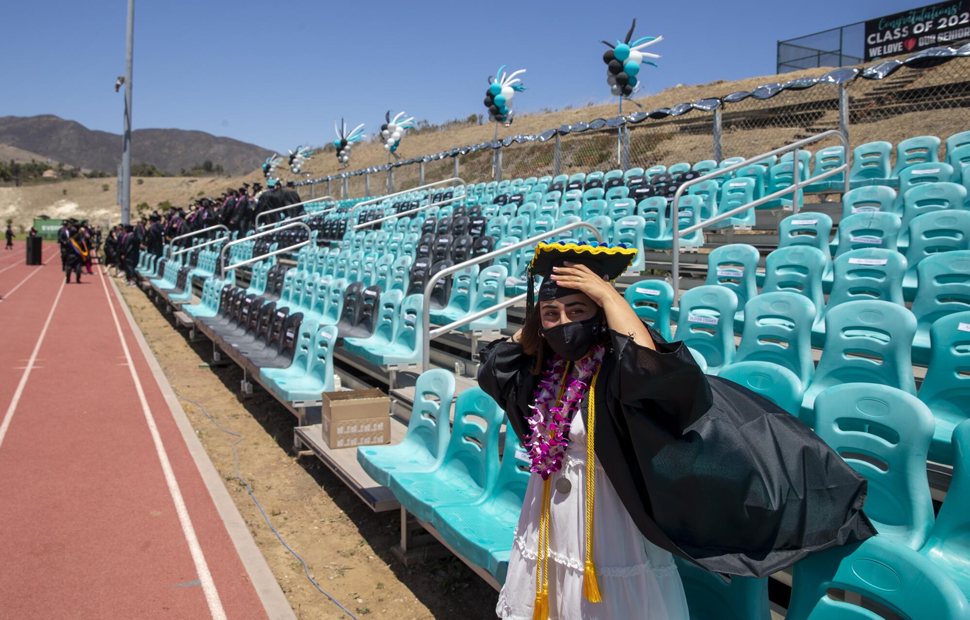 A student's graduation gown billows as she stands on a high school track.