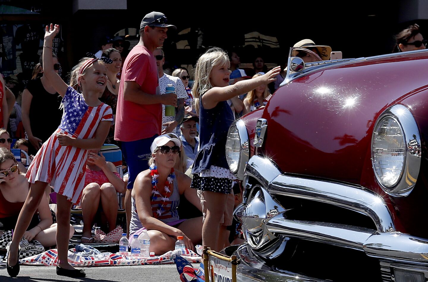 Girls wave at the occupants of vintage automobiles driving down Main Street during the annual Independence Day Parade in Huntington Beach.
