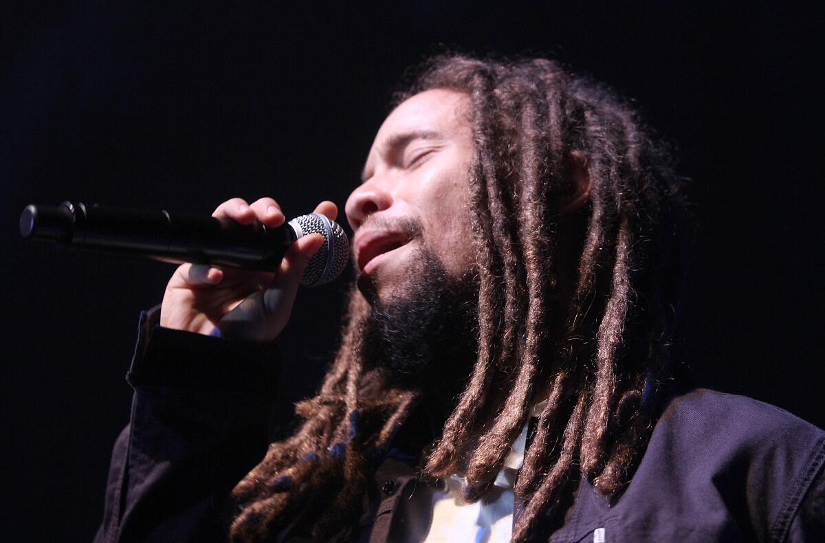 A man with long brown dreadlocks singing into a microphone with his eyes closed