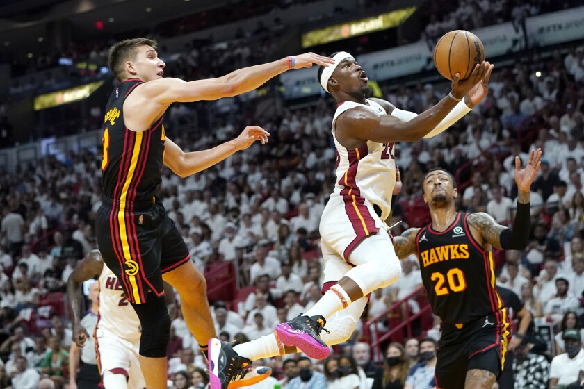Miami Heat forward Jimmy Butler (22) goes to the basket as Atlanta Hawks guard Bogdan Bogdanovic, left, and forward John Collins (20) defend during the first half of Game 1 of an NBA basketball first-round playoff series, Sunday, April 17, 2022, in Miami. (AP Photo/Lynne Sladky)
