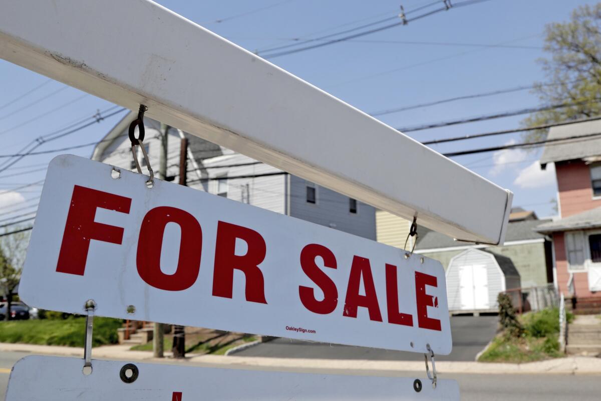 A for sale sign hangs from a post on a suburban street.