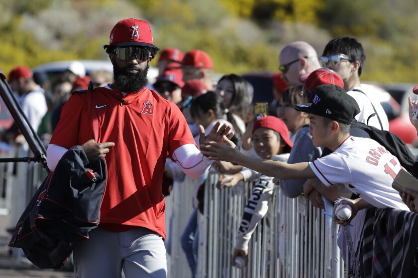 Los Angeles Angels' Brian Goodwin, left, greets a fan during spring training baseball practice, Monday, Feb. 17, 2020, in Tempe, Ariz. (AP Photo/Darron Cummings)
