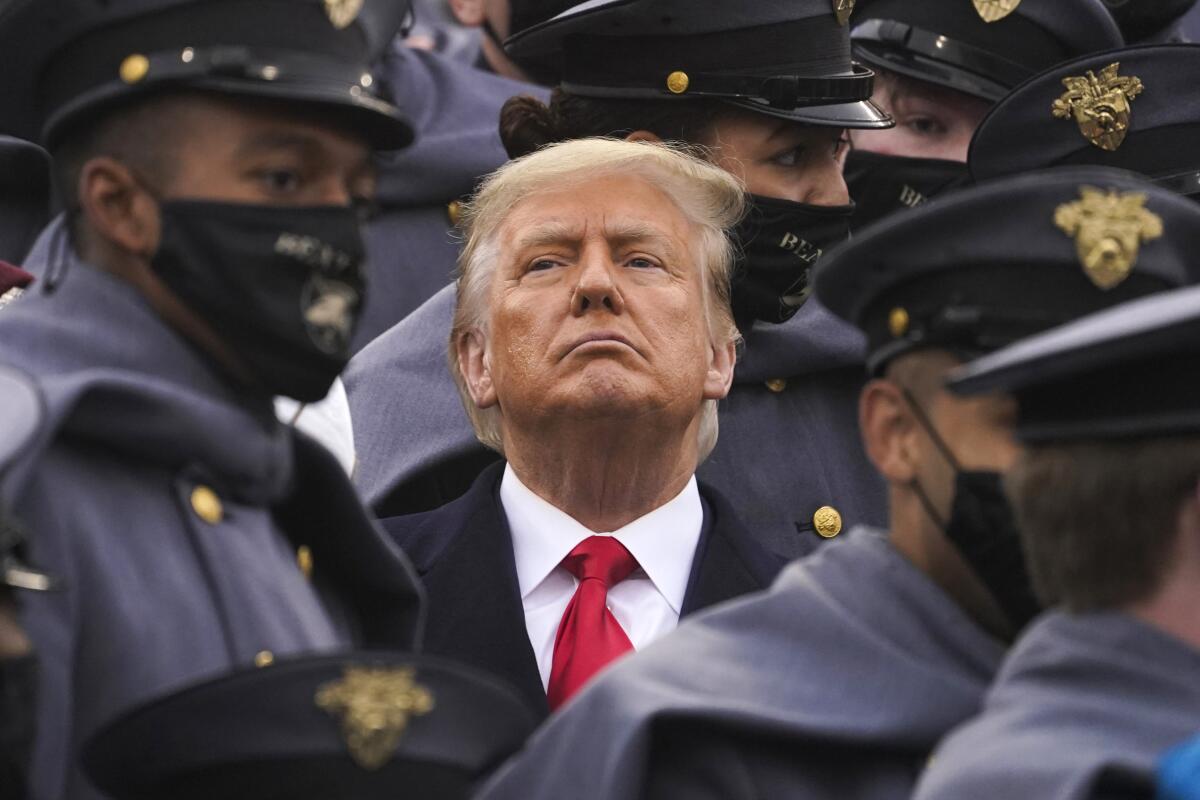 Donald Trump stands with his chin up surrounded by Army cadets.