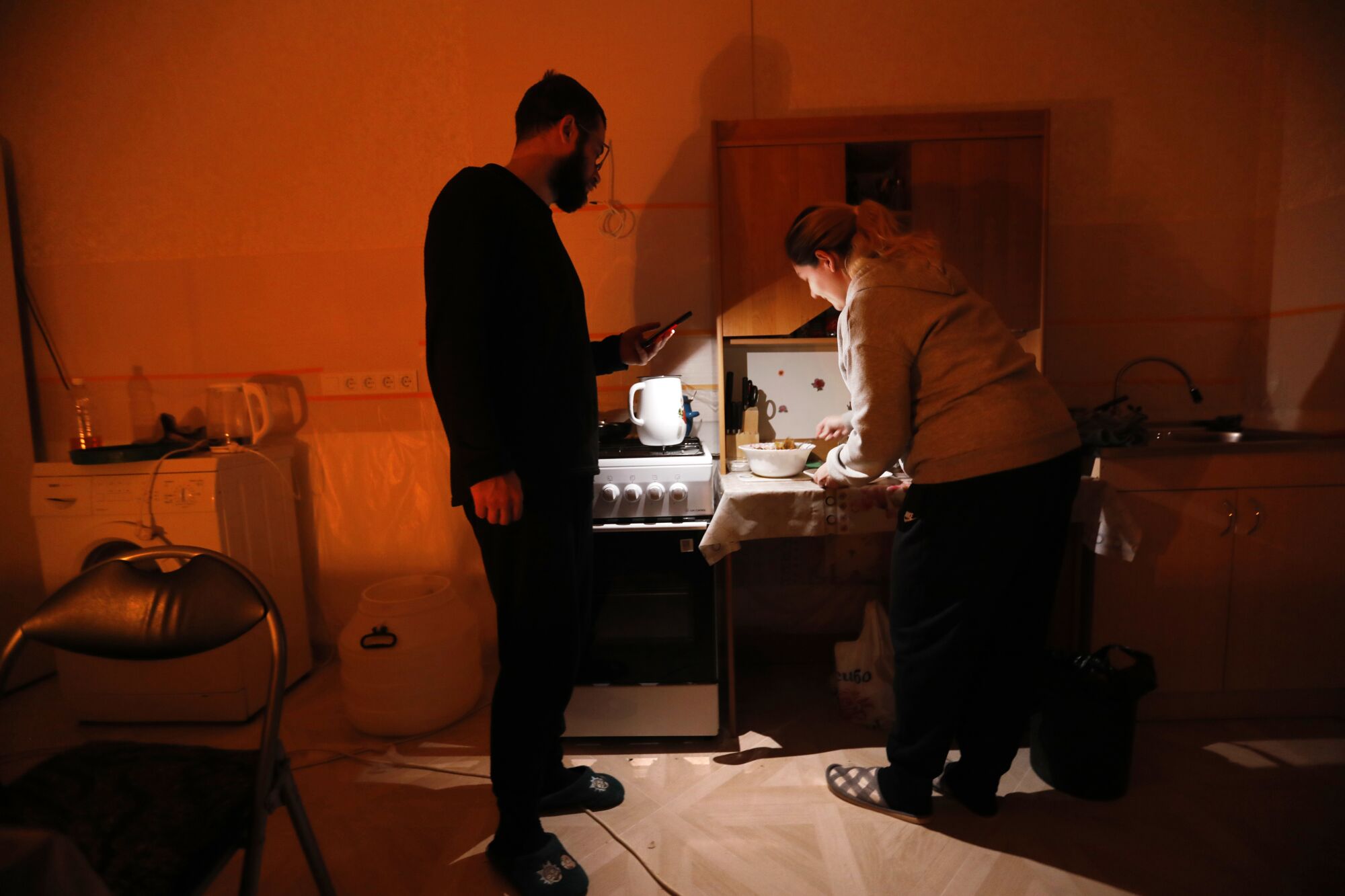 A man in dark clothing, left, uses his cellphone to shine light on a woman preparing food at a table 