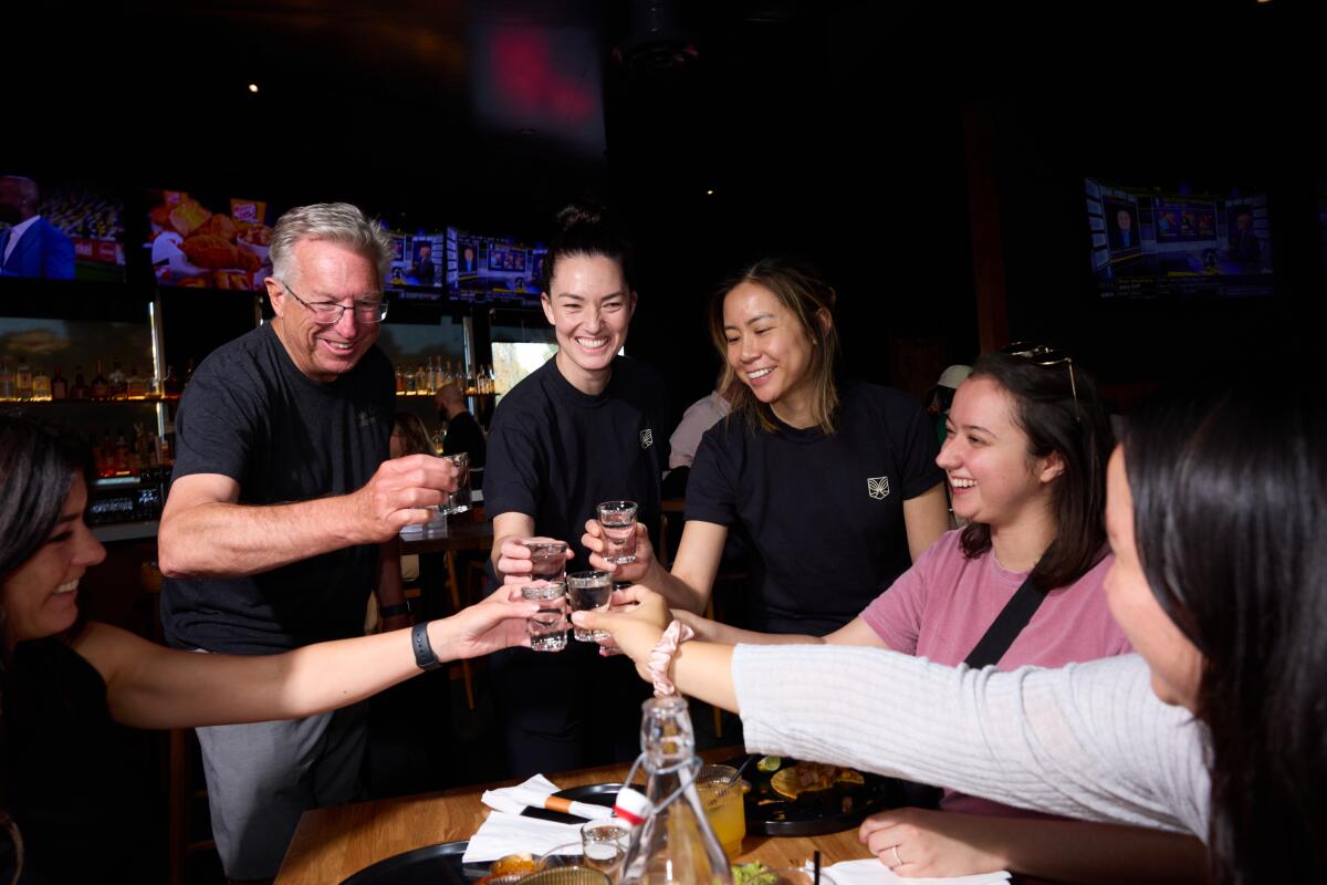 Six people hold their drinks together making a toast.