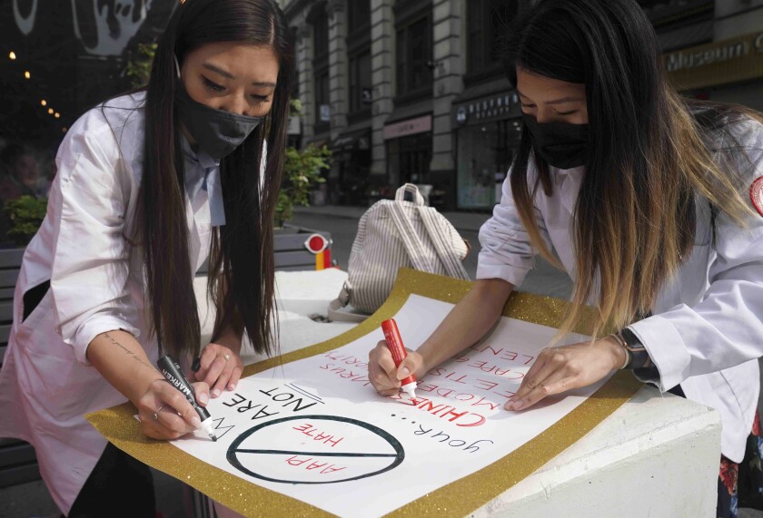 Two masked women work on a poster protesting AAPI hate
