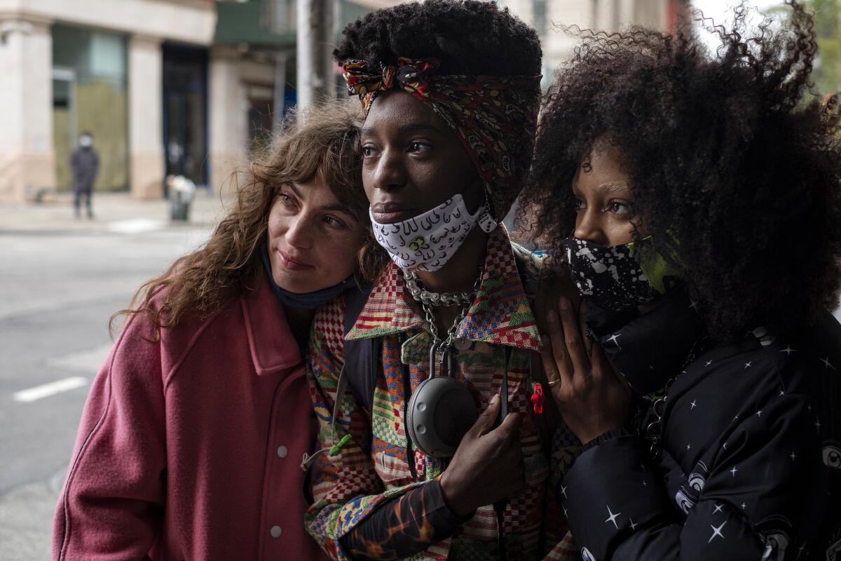 Three women huddle together in jackets on a New York street.