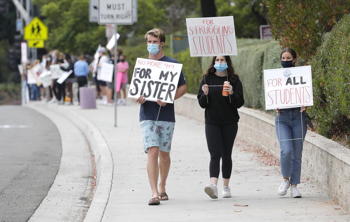 Students Ryan Tanner, Ryann McTague, and Emma Heilman, from left, march along Eastbluff Drive in Newport Beach.