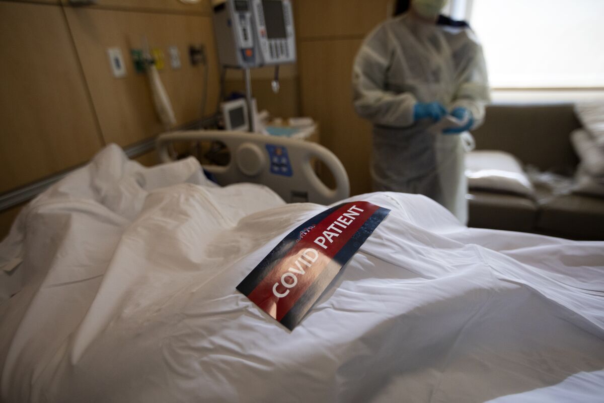 A label that reads "COVID PATIENT" on top of a body covered in a white sheet on a hospital bed