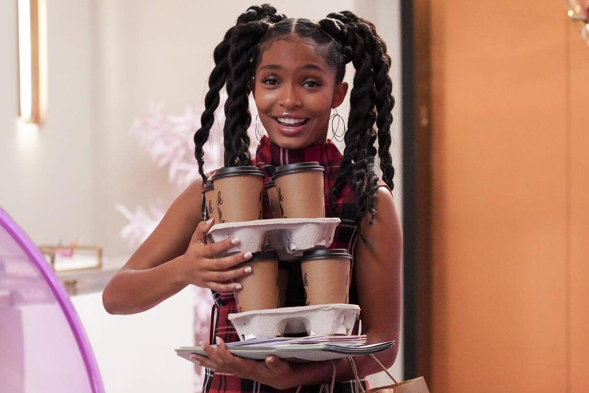 Yara Shahidi holds three trays of paper coffee cups in "Grown-ish."