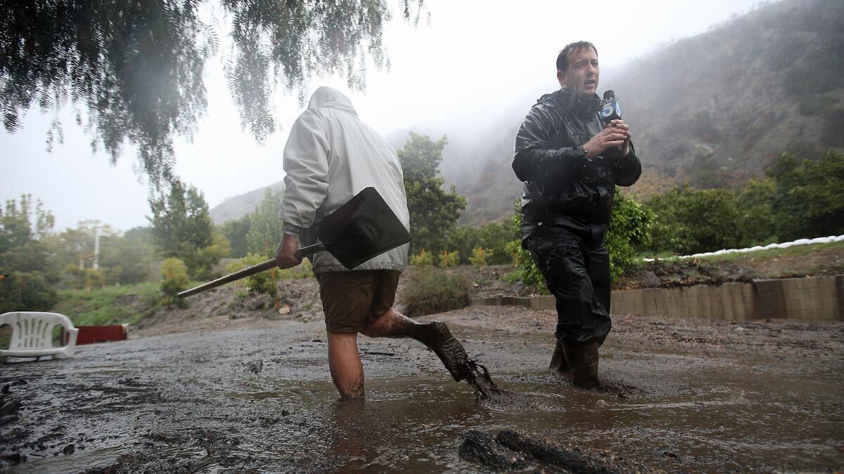 An Azusa man trying to keep drains clear trudges through flowing mud past KTLA reporter Chris Burrous in February 2014.