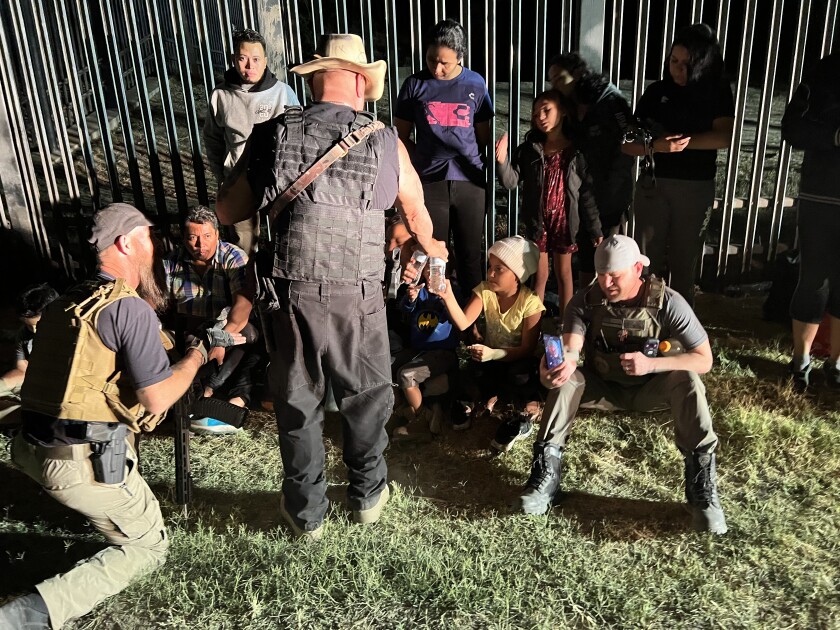 Patriots for America leader Sam Hall, right, talks to migrants as member Shawn Tredway, far left, translates.