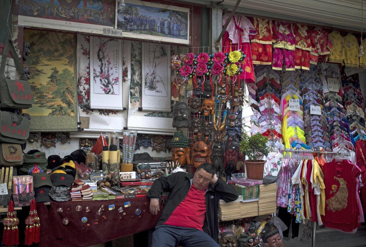 A vendor takes a nap at his store selling a variety of souvenirs along an alley near Qianmen Street, a popular tourist spot in Beijing. A round-trip fare from LAX to China's capital is $758.