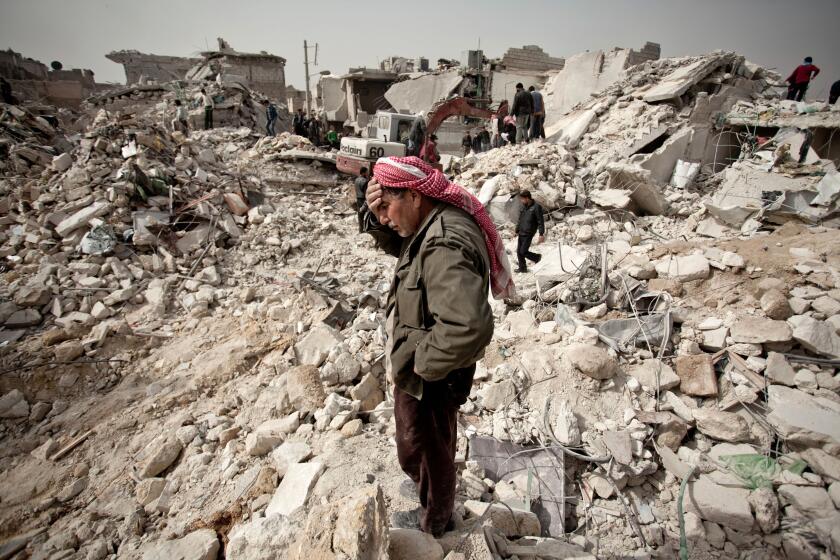 A Syrian man reacts while standing on the rubble of his house