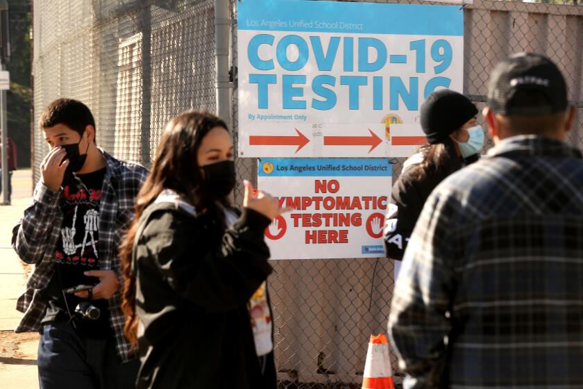 EL SERENO, CA - JANUARY 4, 2022 - - A Health Site Support worker, second from left, directs LAUSD students and staff who wait in line for a COVID-19 test at a walk-up site at the El Sereno Middle School in the El Sereno neighborhood in Los Angeles on January 4, 2022. Students were accompanied by their parents. The Los Angeles school district has ordered coronavirus tests for all students and staff before they return from winter break next week as a new period of high anxiety takes hold among parents and educators amid the explosive surge of the Omicron variant. (Genaro Molina / Los Angeles Times)
