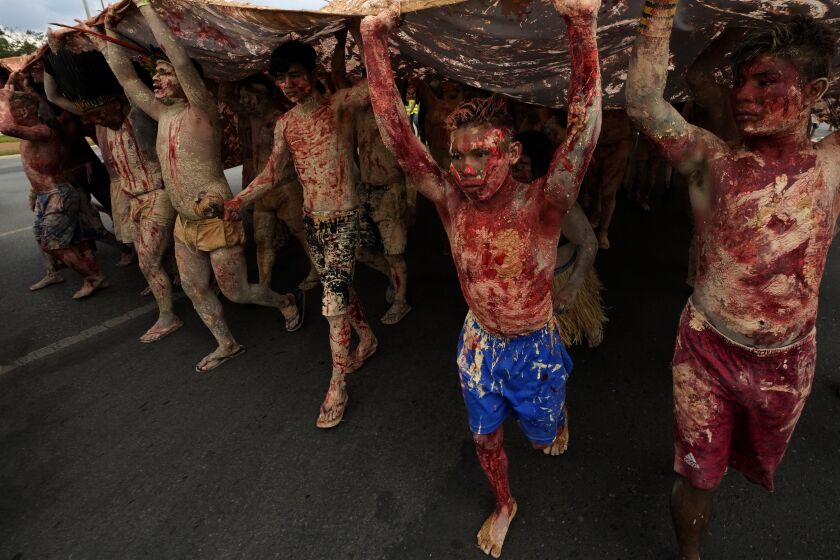 FILE - Indigenous people painted with red ink representing spilled Indigenous blood and clay representing gold, protest against the increase of mining activities that are encroaching on their land, in front of the Ministry of Mines and Energy, in Brasilia, Brazil, April 11, 2022. Some of the world’s biggest mining companies have withdrawn requests for research and production in Indigenous territories of Brazil’s Amazon rainforest, and have repudiated Brazilian President Jair Bolsonaro’s efforts to legalize mining activity in the areas. (AP Photo/Eraldo Peres, File)