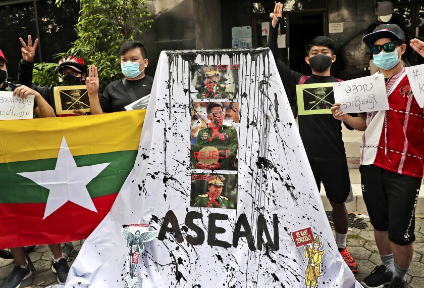 People raise three fingers near a display of paint-spattered photos of three men in uniform and the words Reject and ASEAN