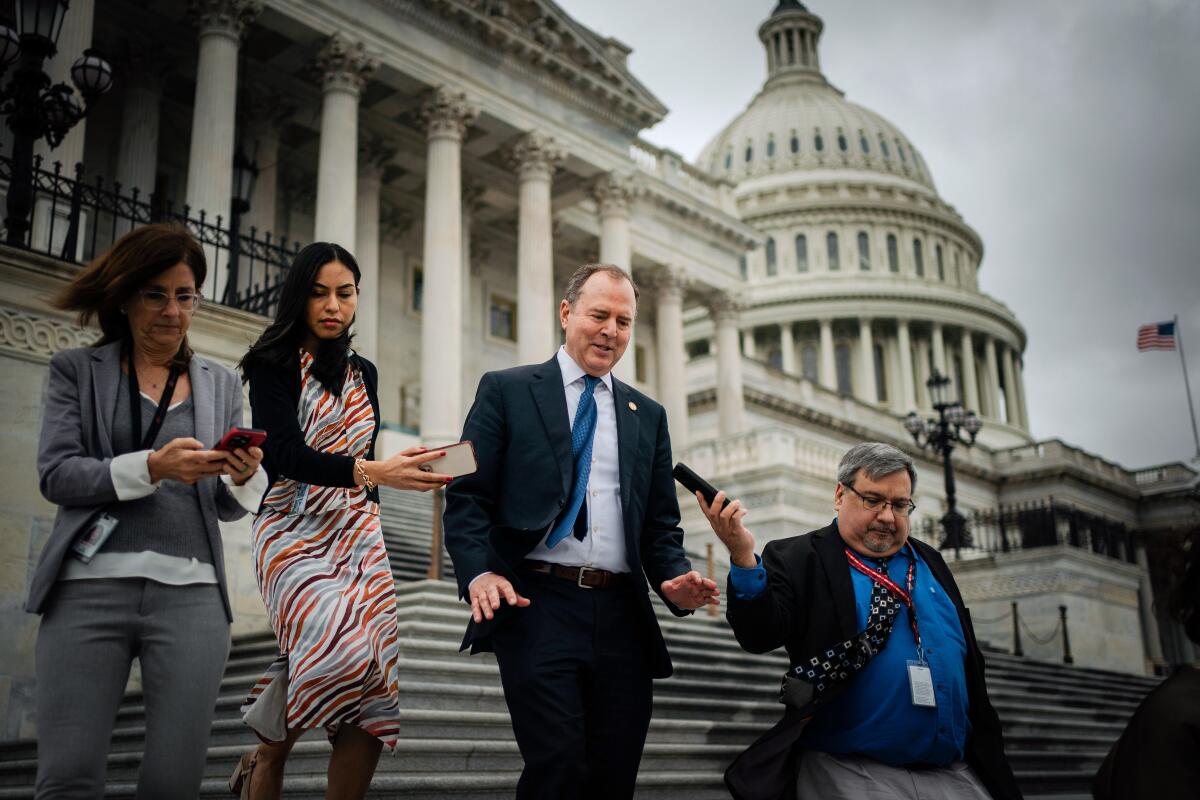 Rep. Adam B. Schiff walking down a stairway outside the U.S. Capitol, talking with three reporters as they walk with him.