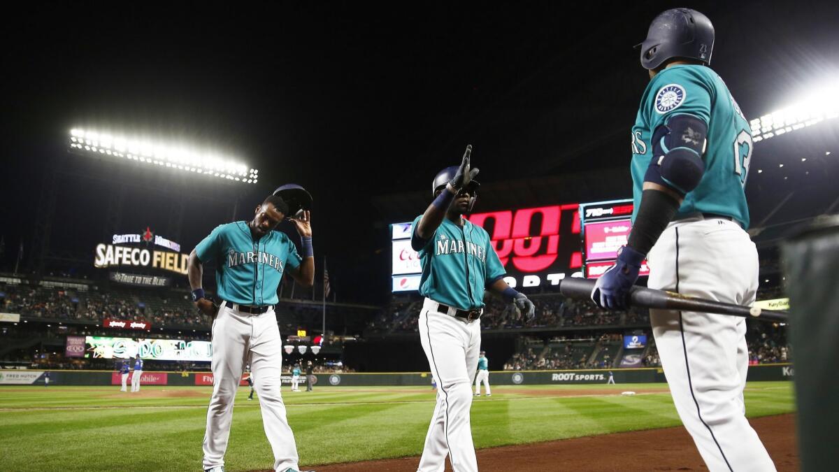 Cameron Maybin (10) of the Seattle Mariners and Guillermo Heredia (5) greet Nelson Cruz (23), right, after scoring on an error.