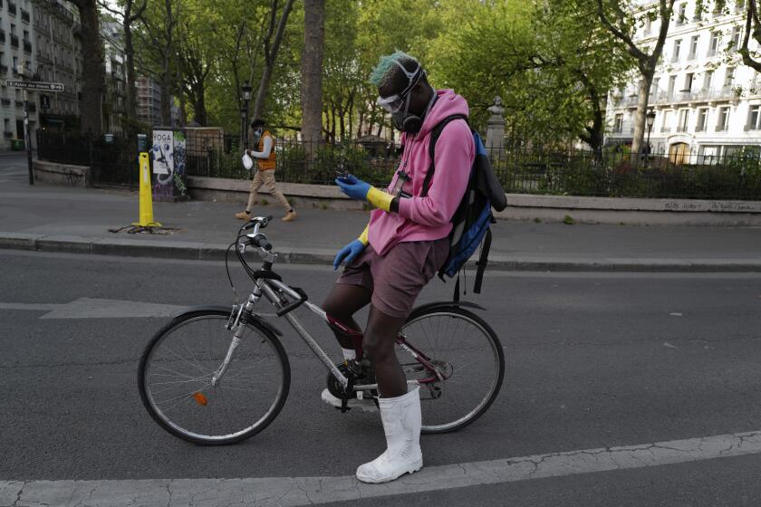 FILE - In this April 20, 2020 file photo, a delivery man, who want to name Moise, wearing protective gear checks his phones during a nationwide confinement in Paris. France is rolling out its contact-tracing app aimed to help containing the spread of the virus as life slowly returns to normal while most of its neighbors, including the UK, Germany, Italy are also about to launch their own technology. (AP Photo/Francois Mori, File)