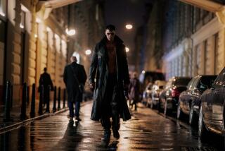 A man in a dark trench coat walks down an urban street.