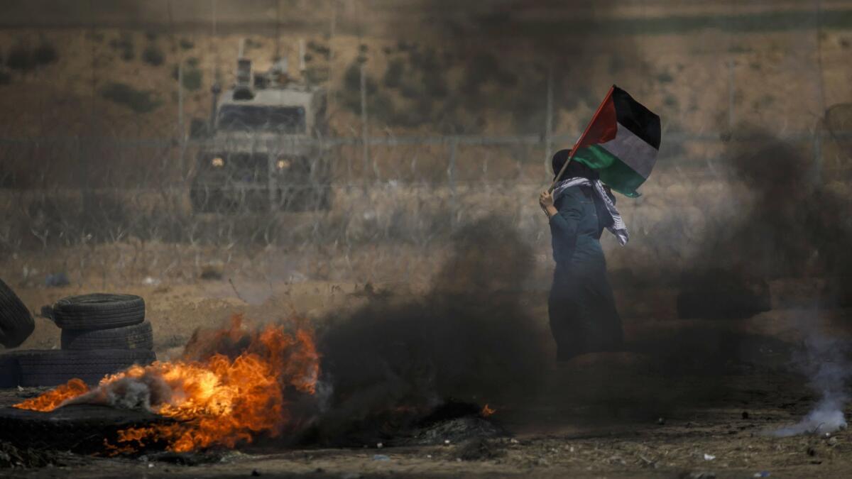 A Gazan woman marches with the Palestinian flag in front of Israeli soldiers during a protest at the border fence separating Israel and the Gaza Strip.
