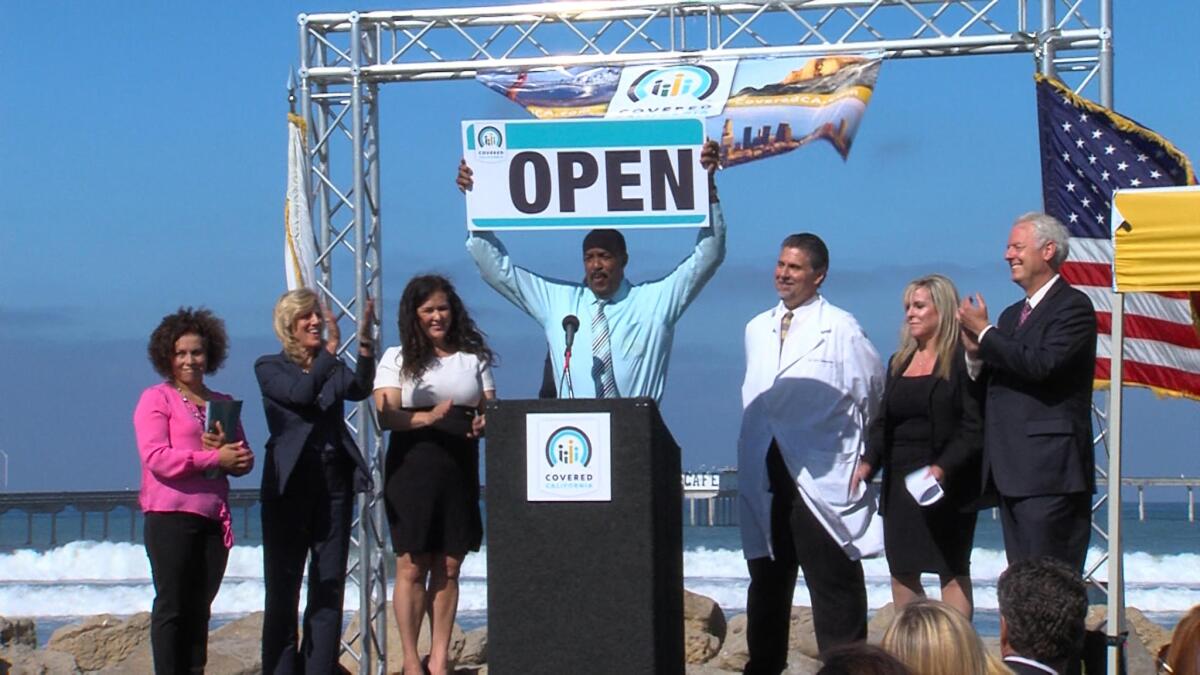 Covered California officials, one with a large "OPEN" sign, announce the state insurance market opening at the beach in 2013.