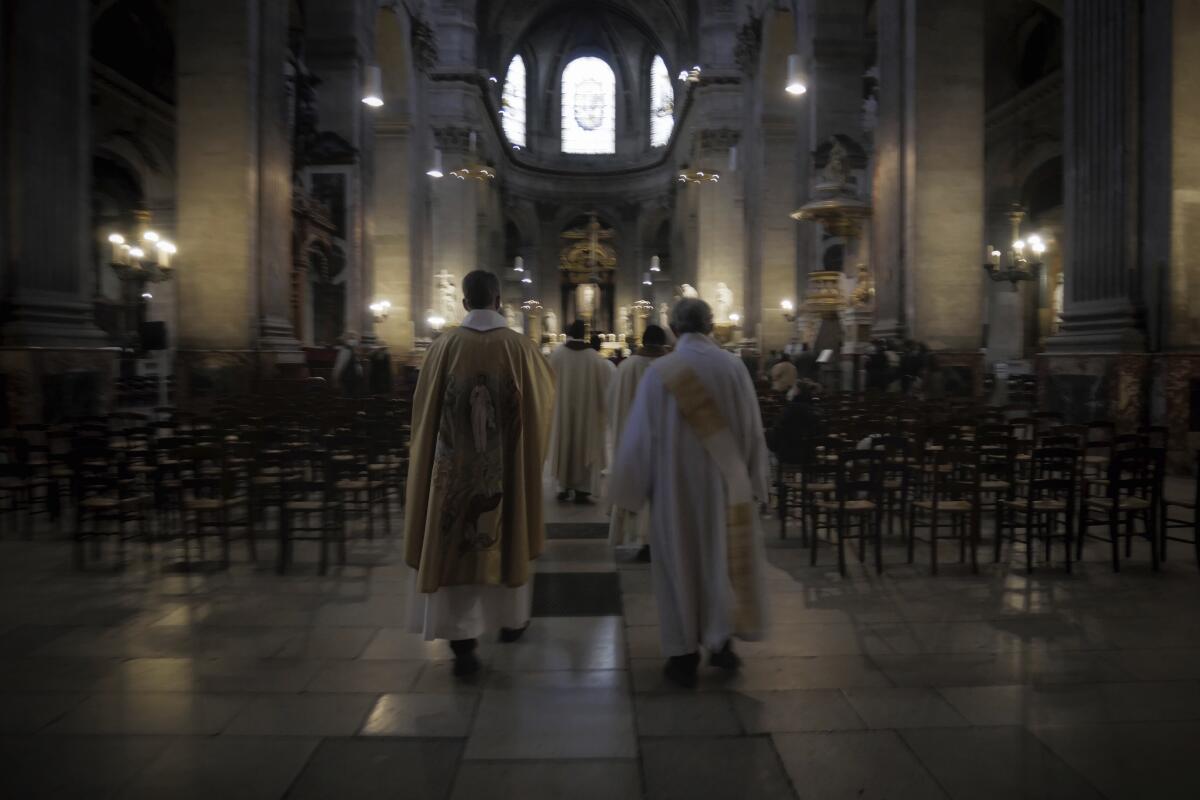 Priest Henri de La Hougue, left, and his assistants celebrate the All Saints Day mass in Saint-Sulpice church, in Paris, Sunday, Nov. 1, 2020. France heightened its security alert amid religious and geopolitical tensions around cartoons mocking the Muslim prophet. (AP Photo/Thibault Camus)