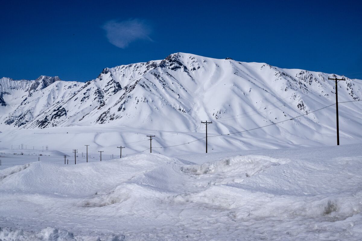 A line of telephone poles are silhouetted against a snowy mountain in the Sierra Nevada