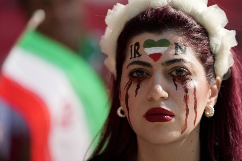 A woman stands on the tribune with her face painted in memory of Mahsa Amini, a woman who died while in police custody in Iran at the age of 22, prior to the World Cup group B soccer match between Wales and Iran, at the Ahmad Bin Ali Stadium in Al Rayyan , Qatar, Friday, Nov. 25, 2022. (AP Photo/Frank Augstein)