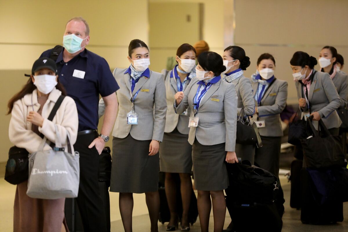 Travelers and a flight crew wait in at an airport terminal.