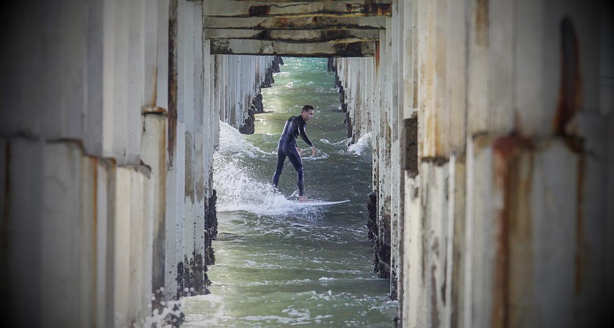 A surfer rides under the Ocean Beach Pier in June 2020.