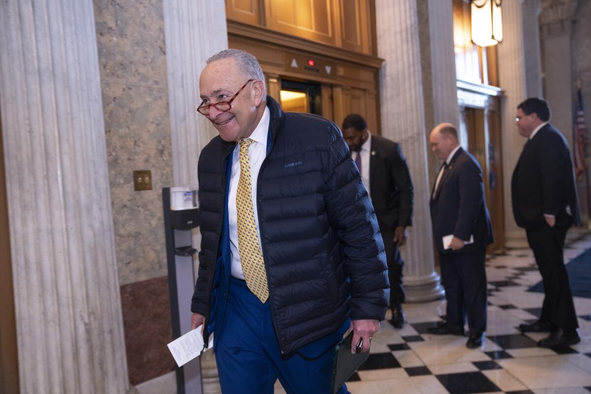 A man with glasses, in a dark puffer jacket, white shirt and yellow tie, smiles in a building lobby 