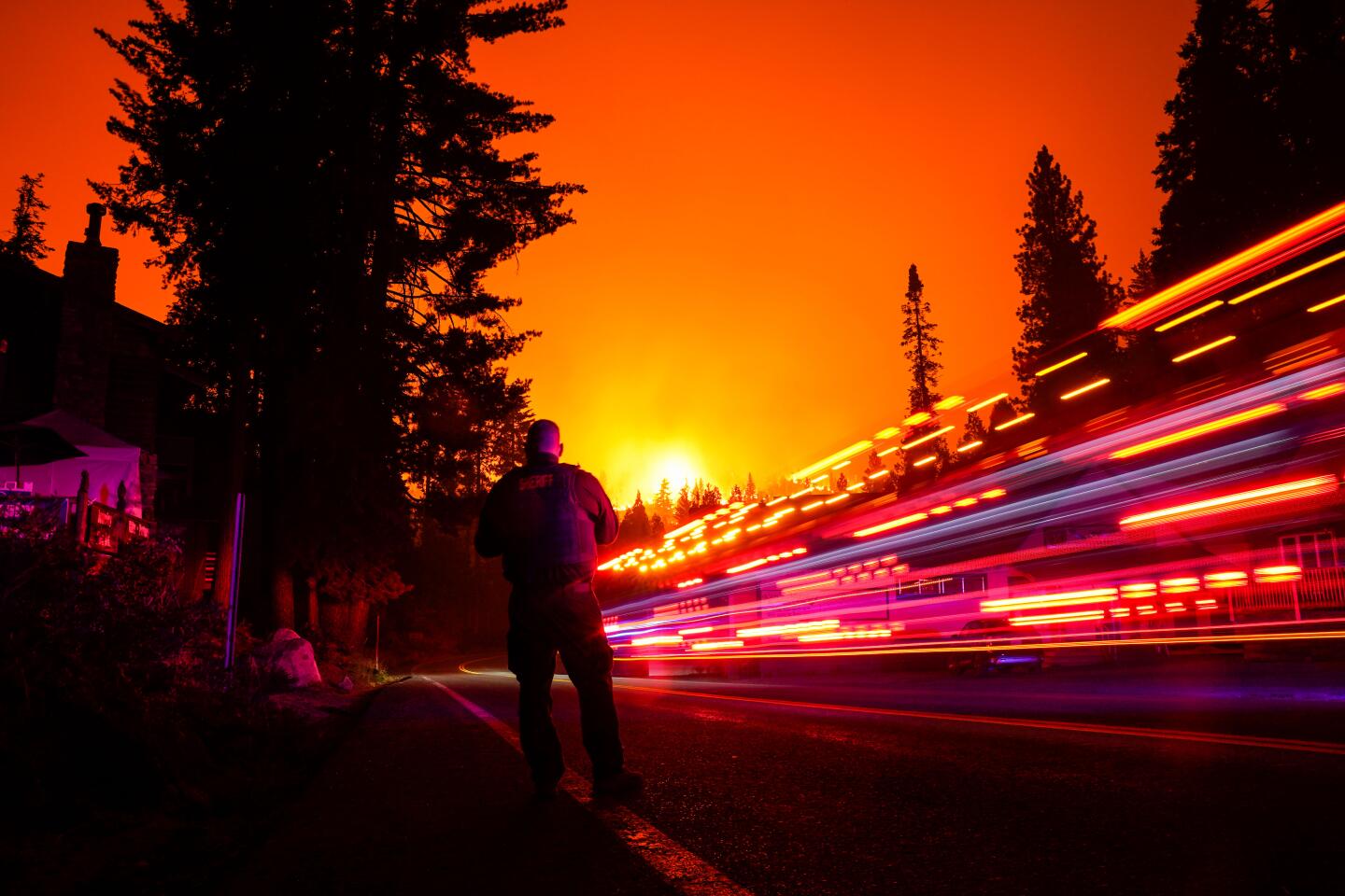 A vehicle streaks by a sheriff's deputy along California 168, with the Creek fire in the background.
