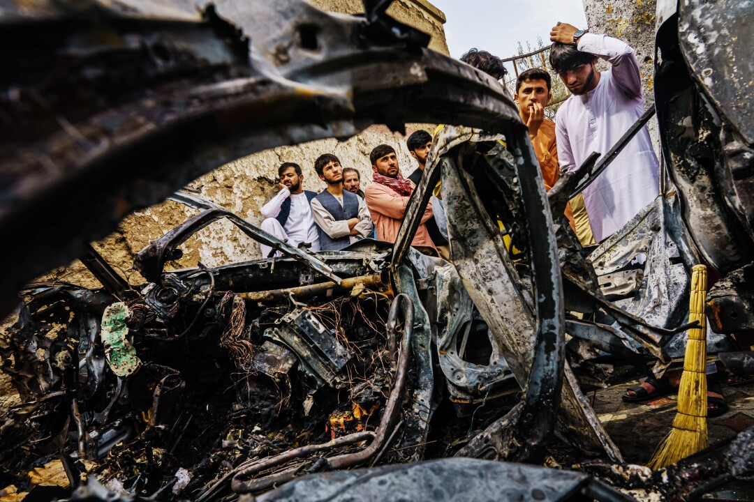  Relatives of the Ahmadi family gather around an incinerated vehicle hit earlier by a drone strike
