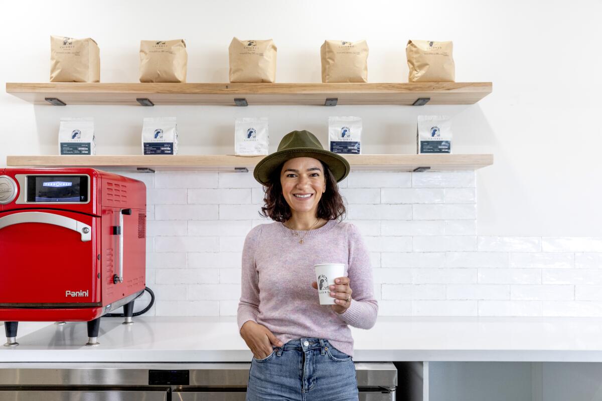 A woman wearing a wide-brim hat holds a paper cup of coffee at Laidrey
