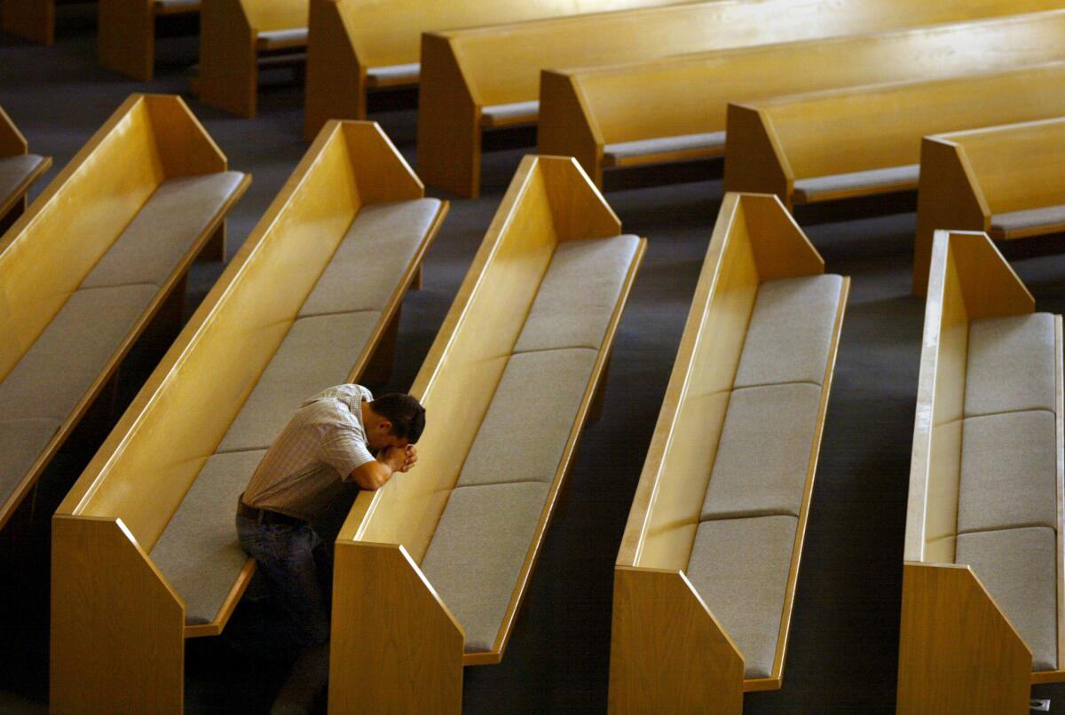 A man prays alone at an Orange County church where five priests were accused of child molestation in 2002.
