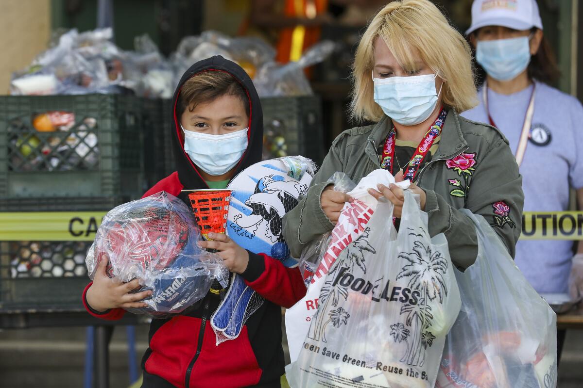 Henry Bernal, left, holding basketball and some other sports items, and his mother Daisy Ledesma leave a Grab and Go meal centers established by LAUSD at Thomas Alva Edison Middle School on Wednesday in Los Angeles.