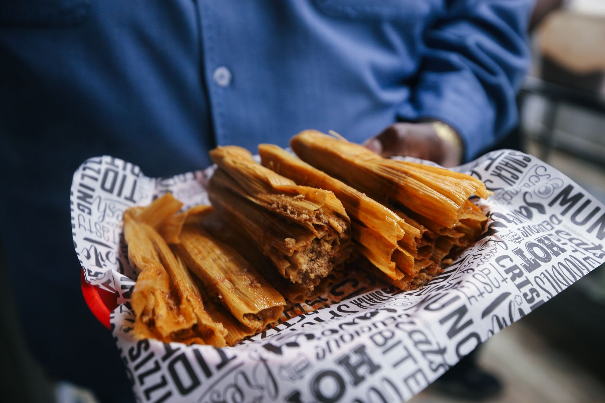 A person holds an order of wrapped and unwrapped tamales.