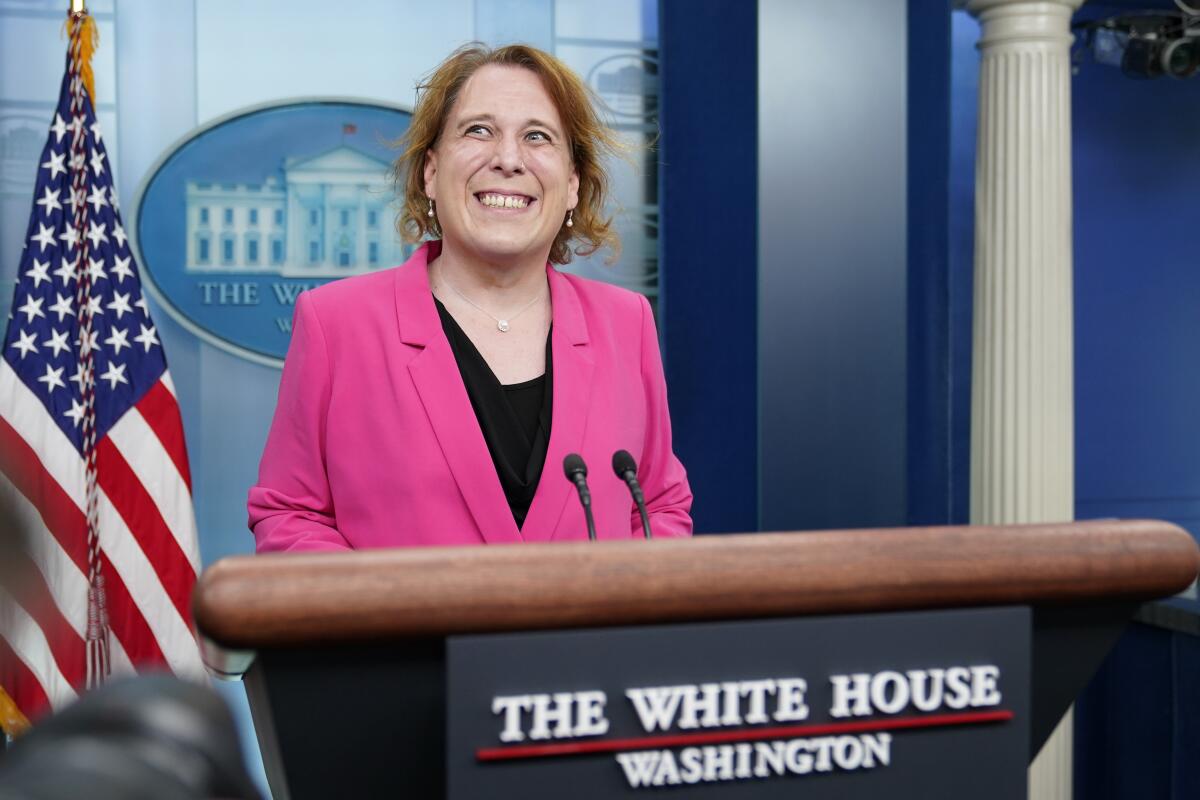 A woman in a pink blazer smiling behind a White House podium