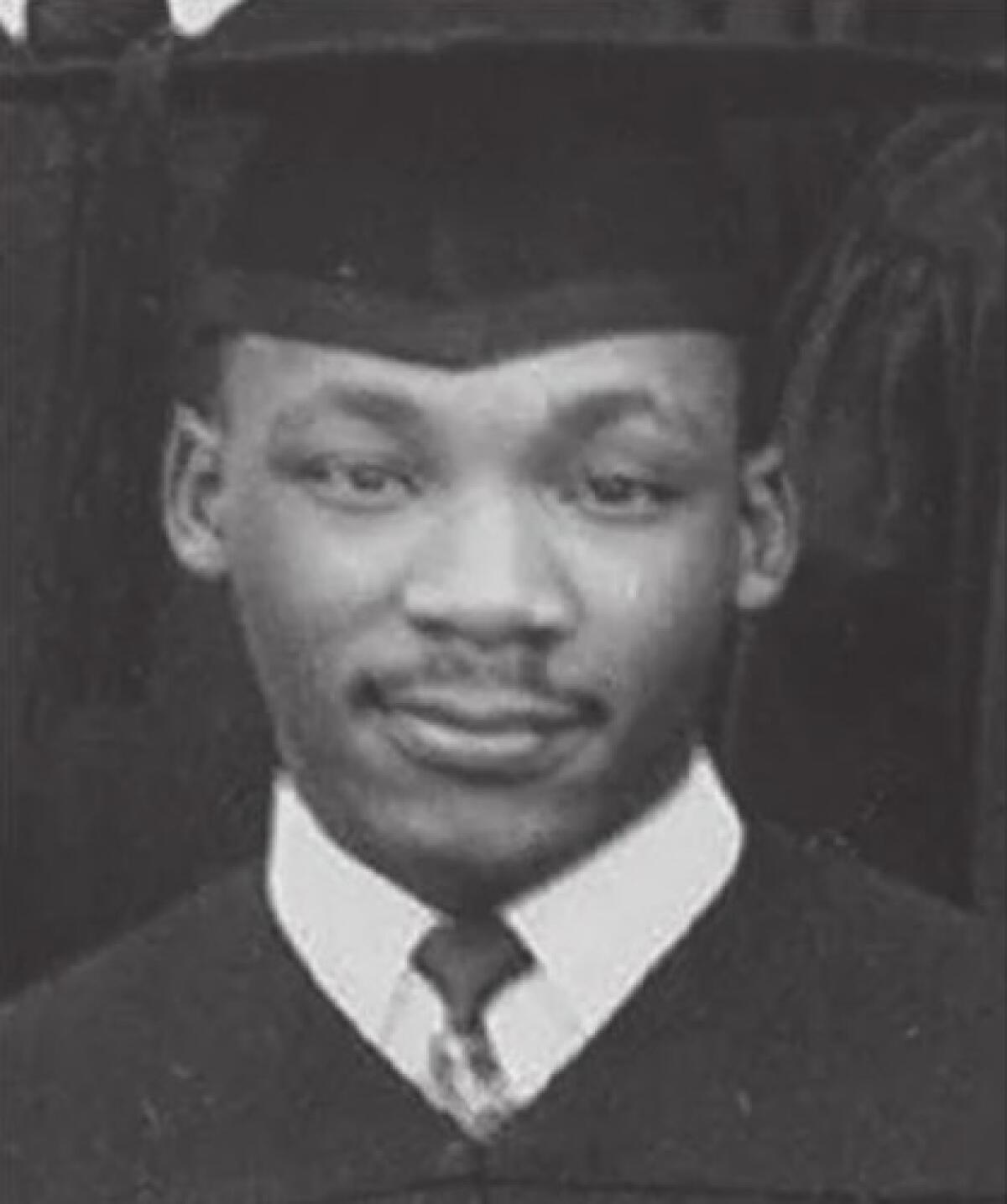 A Black man in a graduation cap and gown and tie.
